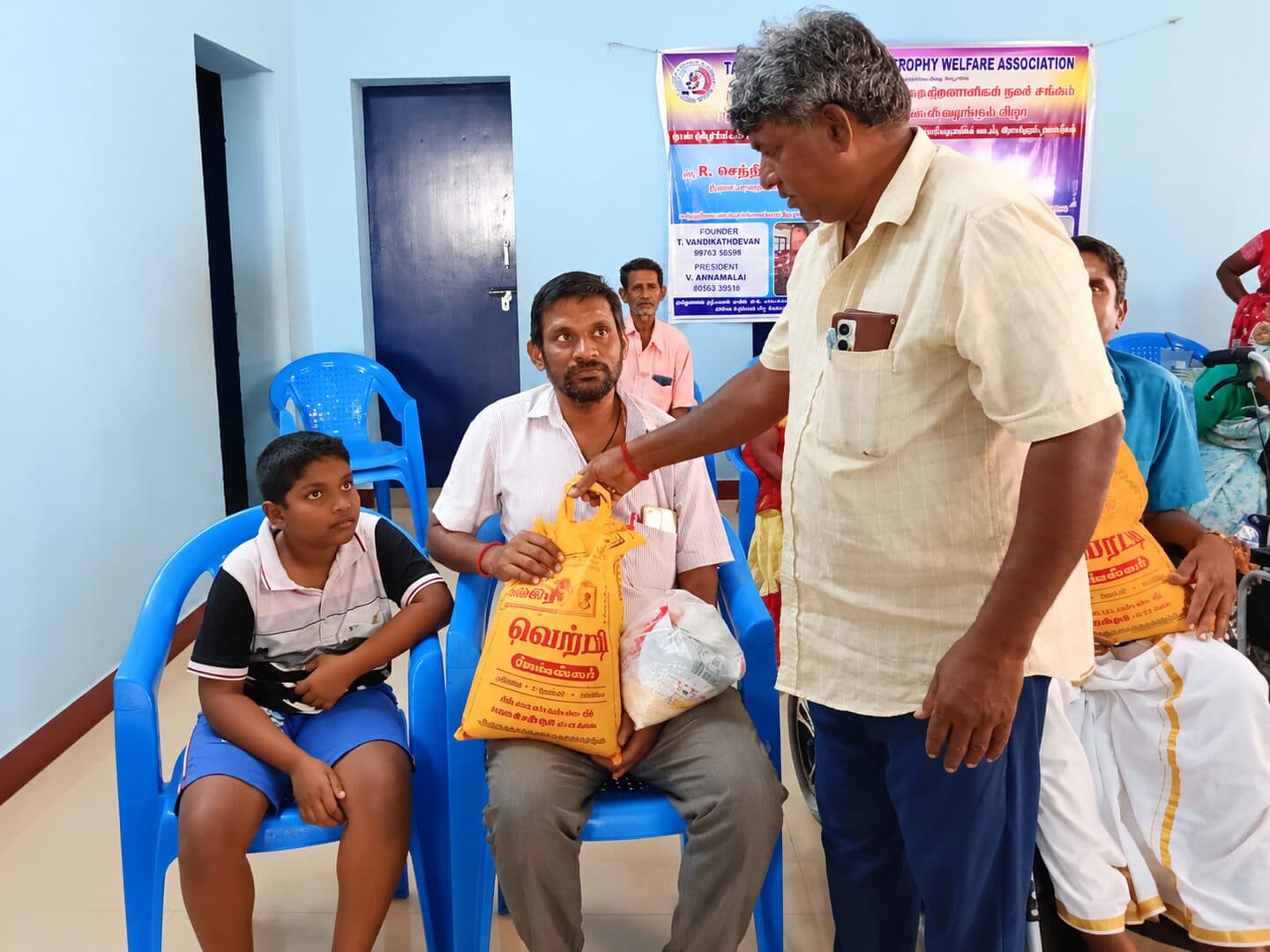 A volunteer handing over a bag of provisions to a seated member as a child looks on